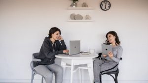 Casual remote work meeting with two women using laptops and tablets at home.